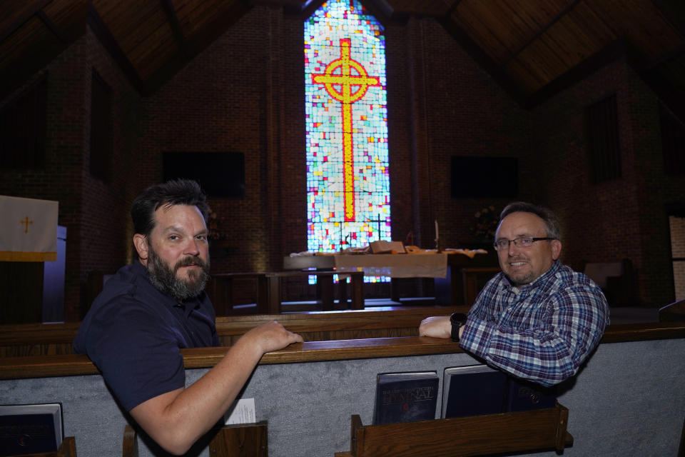 The Rev. Ed McKinney, pastor of Stokesdale United Methodist Church, right, and Michael Hahn, left, pose for a photo in the sanctuary of the church in Stokesdale, N.C., Monday, May 15, 2023. Hahn says he, his wife and daughters have found “a very warm and welcoming environment” in the Stokesdale congregation, with people saying, "We’re glad to have you here, we want to walk through this period with you.” (AP Photo/Chuck Burton)