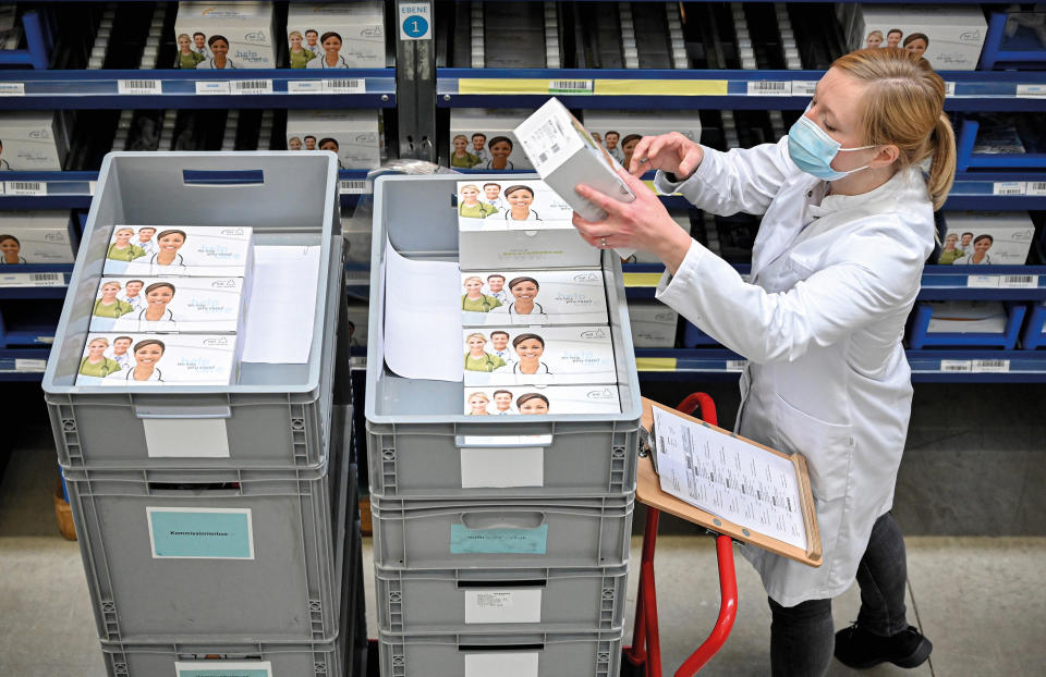 A technical assistant holds a box of COVID vaccines above a trolley full of boxes. (Source: AP)