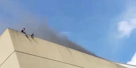 People are seen on the roof of a building as smoke rises during a fire in Davao, the Philippines, in this still image taken a December 23, 2017 social media video. Ashley Nicole Avila Rafaela/via REUTERS