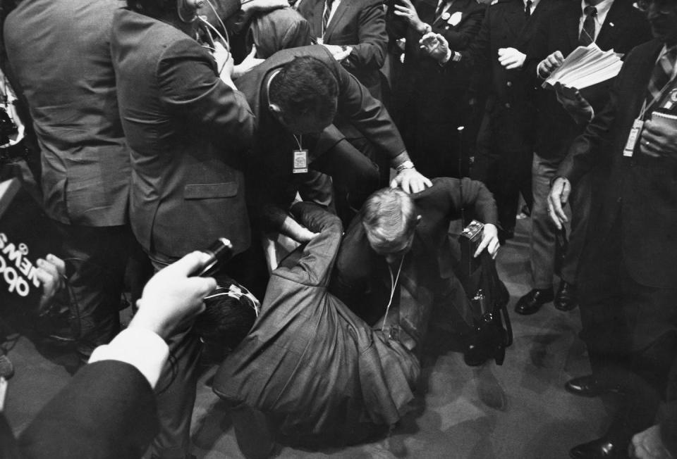 A group of men in suits surround someone on the floor.