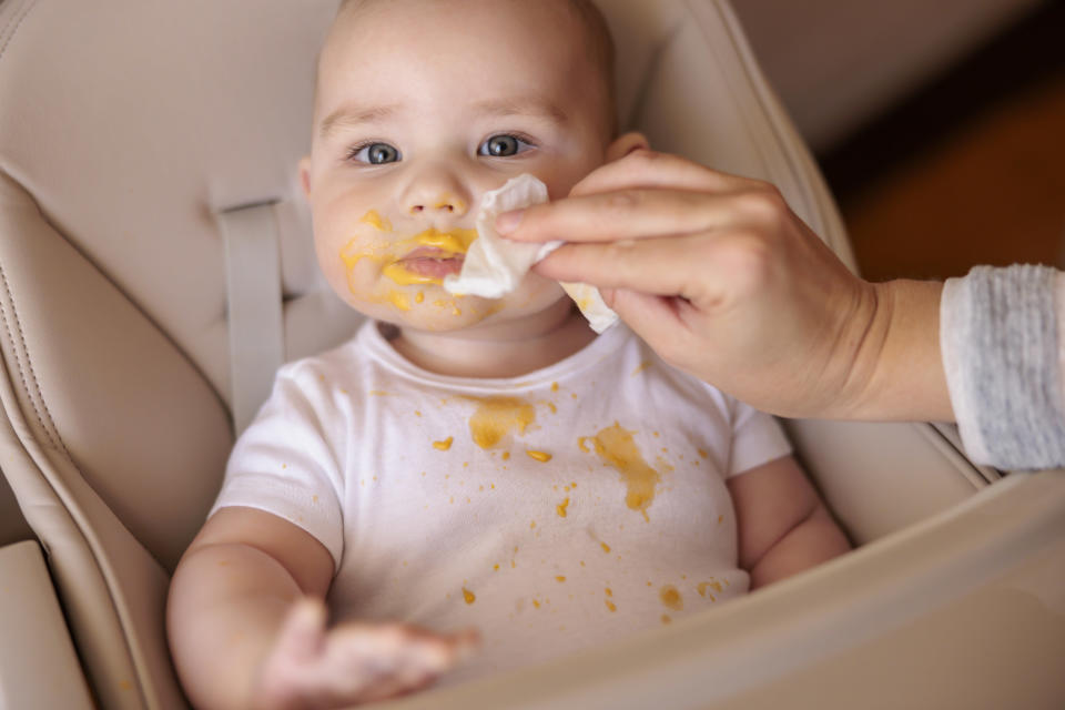 person wiping baby's face with a baby wipe during a messy feed