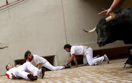 Sergio Colas (C) moves away from the path of an El Pilar fighting bull after falling at the entrance to the bullring during the seventh running of the bulls at the San Fermin festival in Pamplona, northern Spain, July 13, 2011. REUTERS/Susana Vera/Files