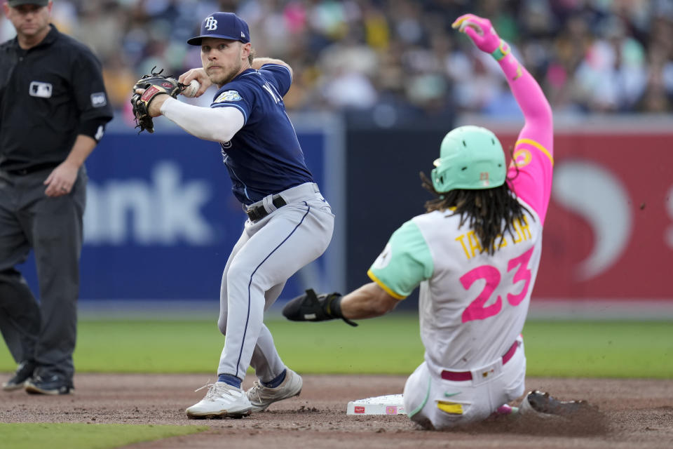 Tampa Bay Rays second baseman Taylor Walls, left, throws to first for the double play as San Diego Padres' Fernando Tatis Jr. slides in late to second during the first inning of a baseball game Friday, June 16, 2023, in San Diego. San Diego Padres' Manny Machado was out at first on the play. (AP Photo/Gregory Bull)