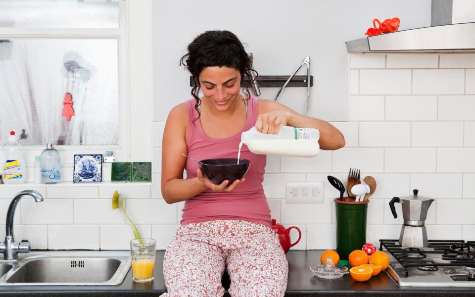 Woman pouring milk over cereal in kitchen
