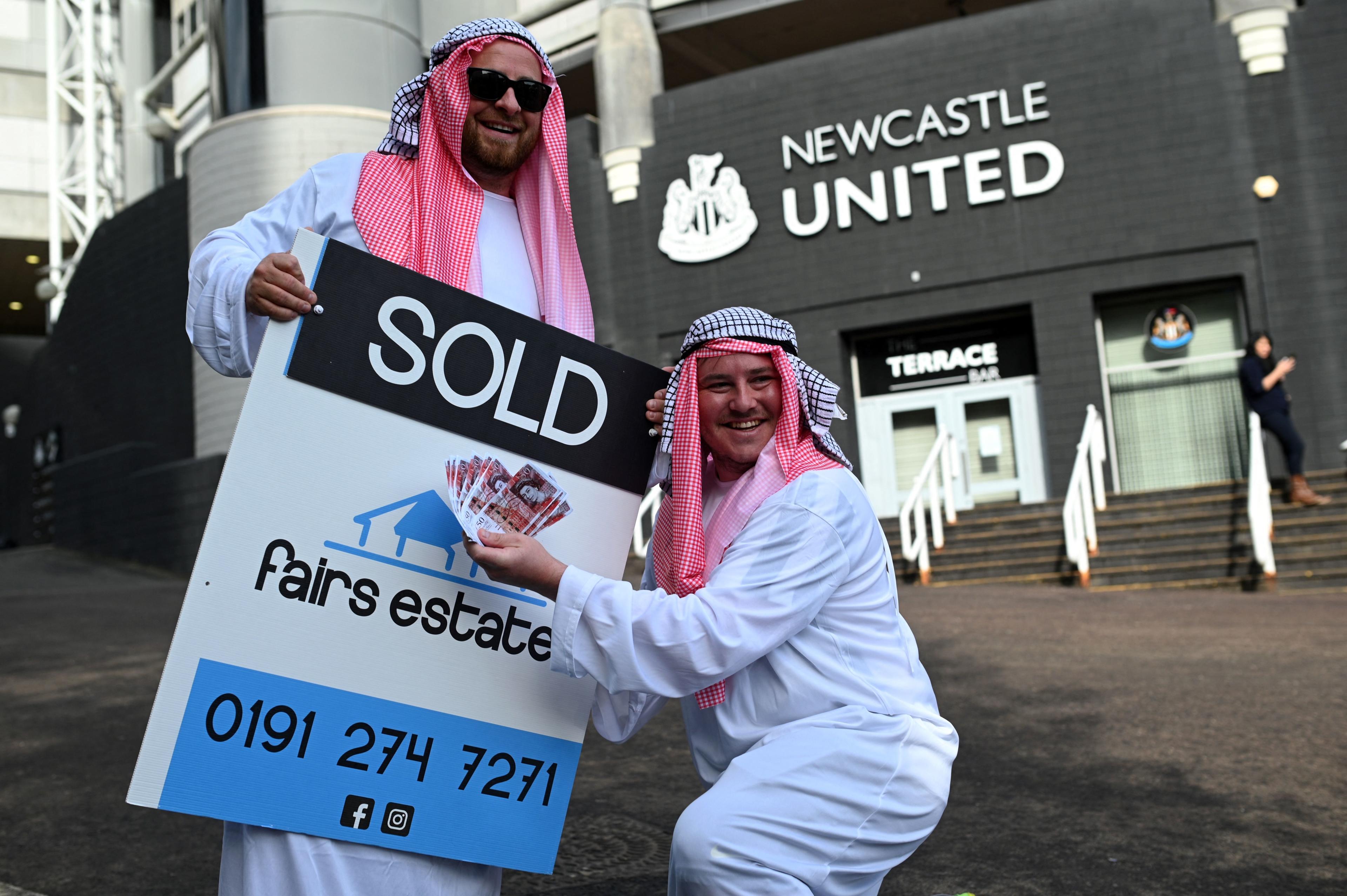 Newcastle United supporters dressed in robes pose with 'sold' placards as they celebrate the sale of the club to a Saudi-led consortium, outside the club's stadium at St James' Park in Newcastle upon Tyne in northeast England on October 8, 2021. - A Saudi-led consortium completed its takeover of Premier League club Newcastle United on October 7 despite warnings from Amnesty International that the deal represented 
