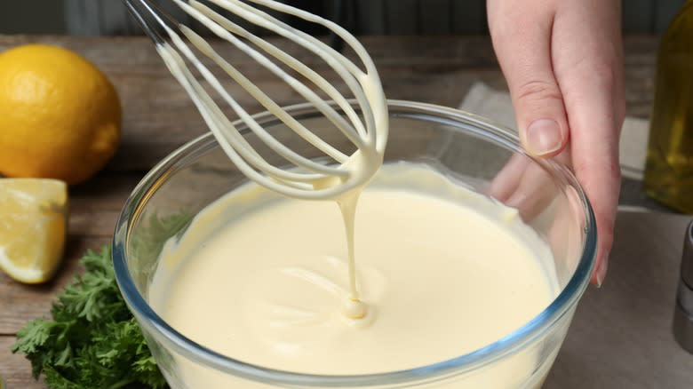 hand whisking creamy salad dressing in a glass bowl