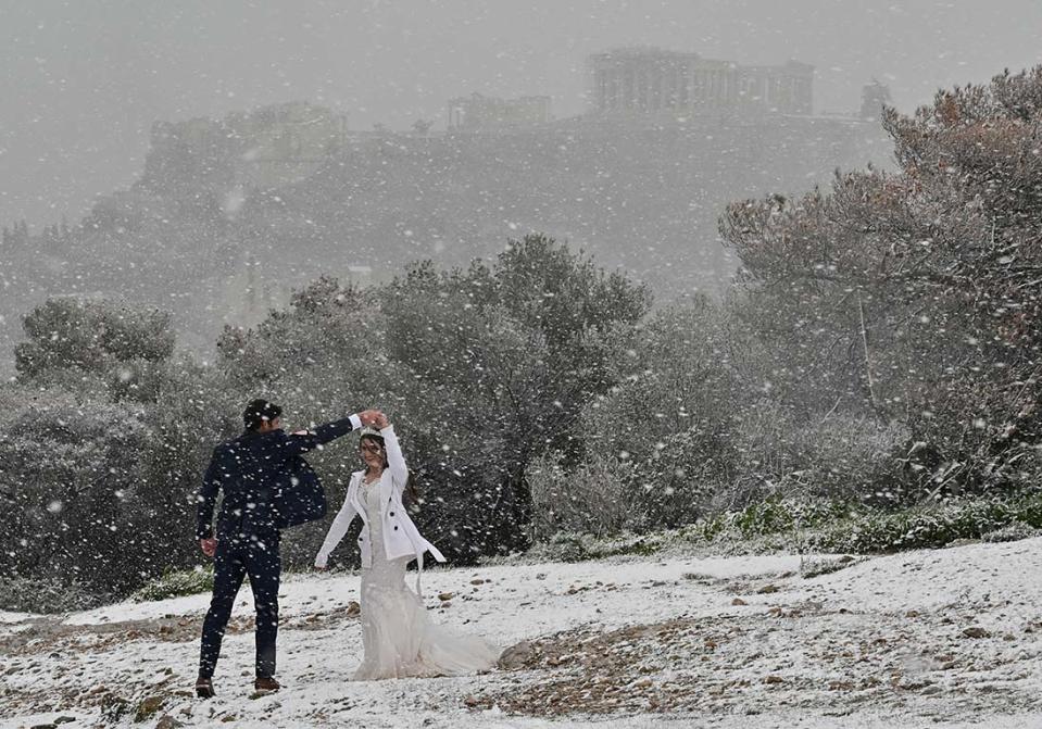 De jeunes mariés dansent dans la neige avec pour fond, l'Acropole