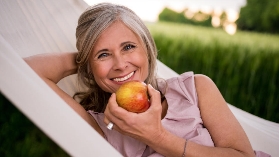 A woman lying in a hammock holding an apple, which is one of the best cortisol-lowering foods