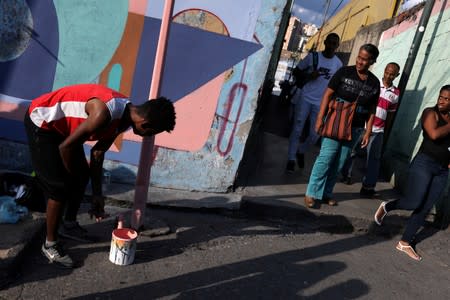 Neighbors looks at a man as he helps artist Fabian Solymar to paint a mural in a wall of Petare slum, in Caracas