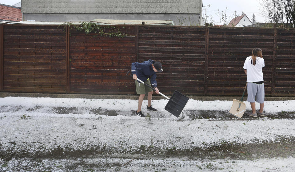 Residents shovel hail from the sidewalk in Kissing, Germany, Saturday Aug. 26, 2023. A storm with large hailstones damaged four-fifths of the buildings in a small town in the southern German state of Bavaria, local authorities said Sunday. The storm swept across the southern part of Bavaria on Saturday. In Kissing, just outside Augsburg, police said 12 people were injured when a beer tent that they were trying to put up was blown over. (Karl-Josef Hildenbrand/dpa via AP)