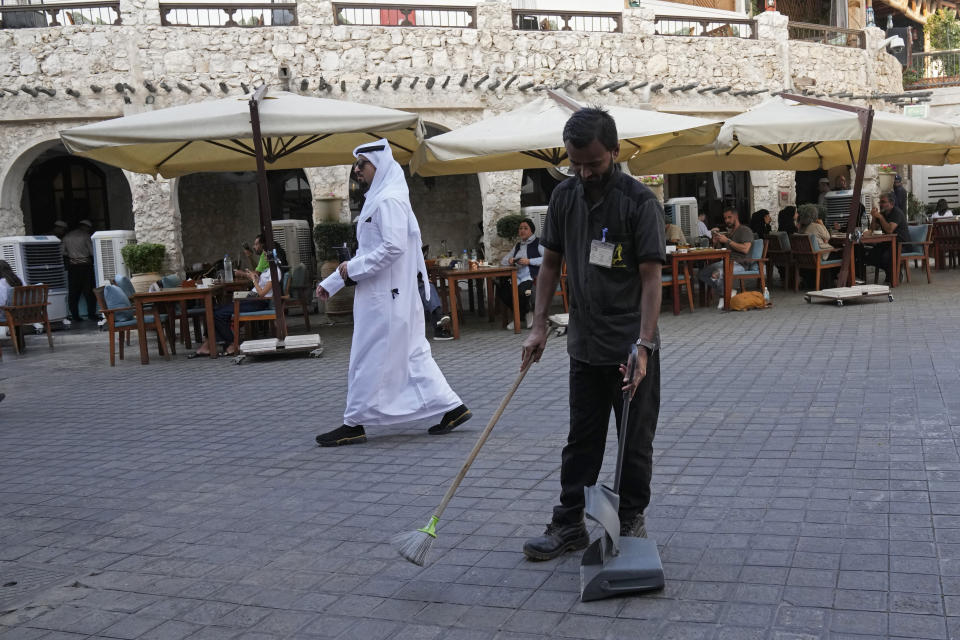 A migrant worker from Nepal removes trash as a man in Arabic attire walks past at Souk Waqif in Doha, Qatar, Tuesday, Jan. 16, 2024. The plight of migrant workers in Qatar came under the spotlight for more than decade after the gas-rich Middle Eastern emirate was awarded the World Cup in 2010. Workers labored in the searing heat to build over $200 billion worth of stadiums and infrastructure that helped make the tournament such a success. (AP Photo/Aijaz Rahi)