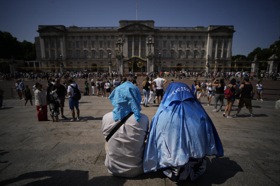People sit covering their heads from the sun after a scaled down version of the Changing of the Guard ceremony took place outside Buckingham Palace, during hot weather in London, Monday, July 18, 2022. Britain's first-ever extreme heat warning is in effect for large parts of England as hot, dry weather that has scorched mainland Europe for the past week moves north, disrupting travel, health care and schools. (AP Photo/Matt Dunham)