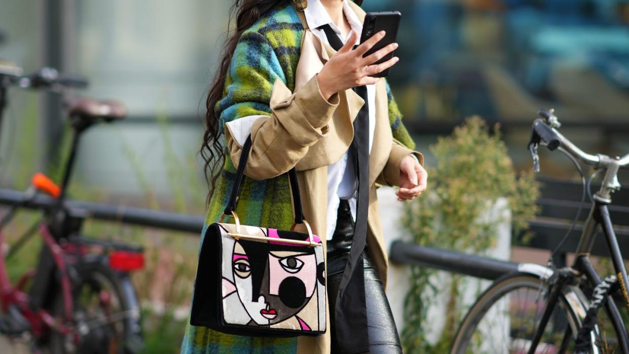 a woman wearing sunglasses and a green and beige coat holding a phone