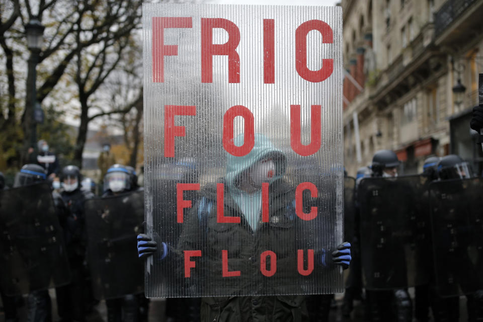 A demonstrator holds a poster reading "Too much money, Fuzzy cops" during a protest against a proposed bill , Saturday, Dec.12, 2020 in Paris. The bill's most contested measure could make it more difficult for people to film police officers. It aims to outlaw the publication of images with intent to cause harm to police. The provision has caused such an uproar that the government has decided to rewrite it. Critics fear the law could erode press freedom and make it more difficult to expose police brutality. (AP Photo/Lewis Joly)