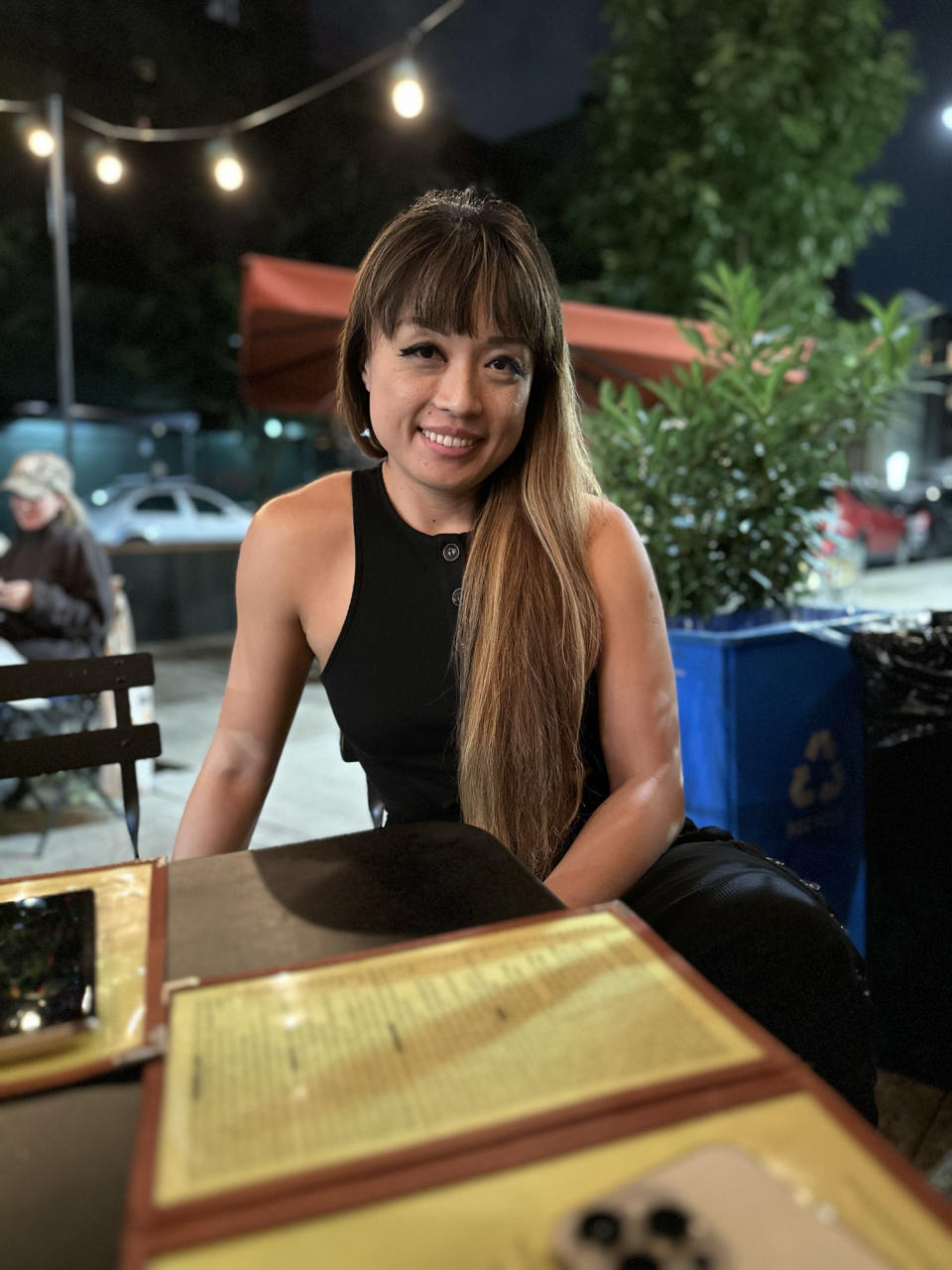 <p>A Portrait mode photo from the iPhone 14 Pro's rear main camera of a woman sitting at a table in an outdoor restaurant.</p>
