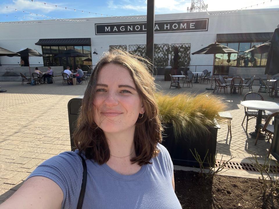 A woman takes a selfie in front of a building that says "Magnolia Home."