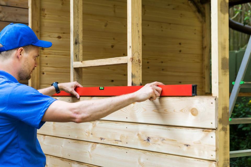 man-uses-a-level-to-construct-a-wooden-shed