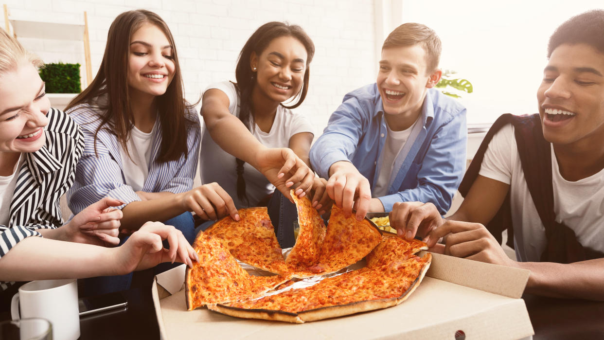 Time for snack. Happy students eating pizza and chatting at home