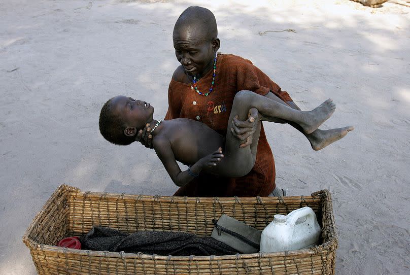 A mother gently places her son in a basket as she takes him to a Medecins Sans Frontieres clinic after he contracted malaria, in Lankien, Southern Sudan, 2005.