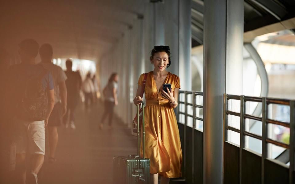 woman walking with suitcase looking at phone