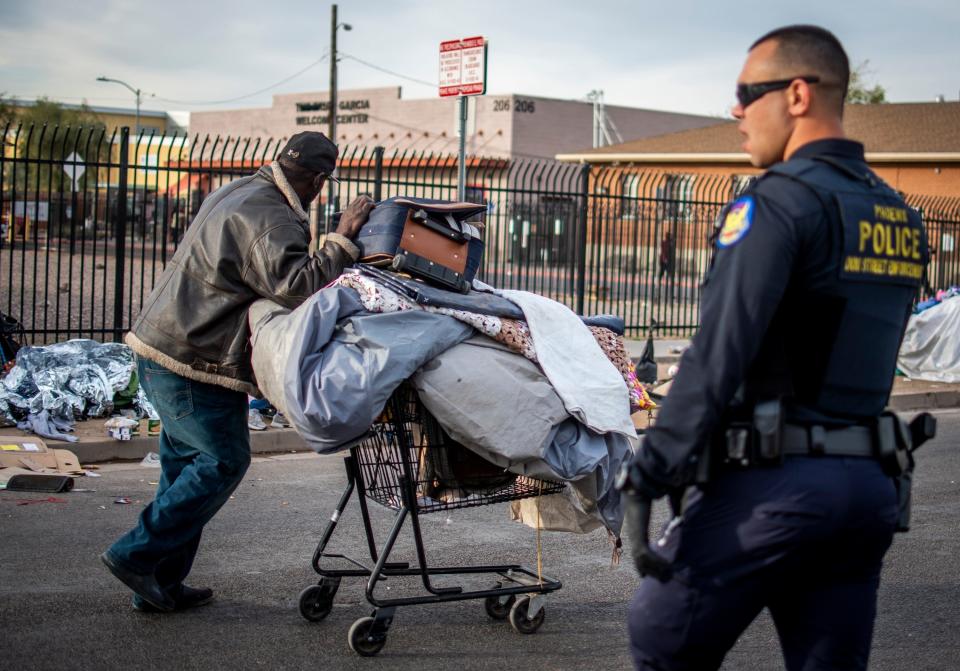 A man experiencing homelessness moves his belongings by a Phoenix police officer.