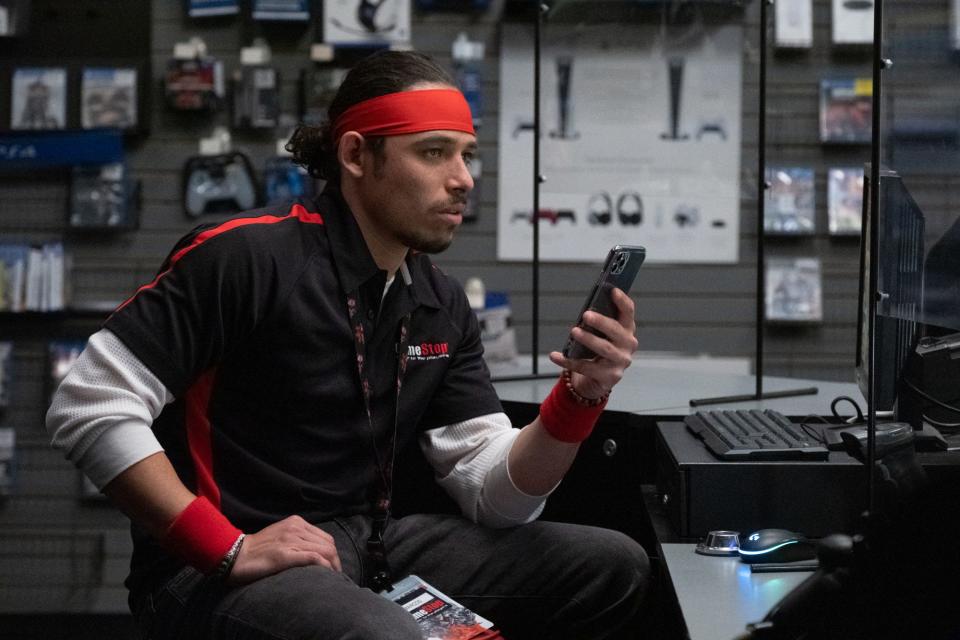 Anthony Ramos sits in a chair while on his phone as a GameStop employee in "Dumb Money."