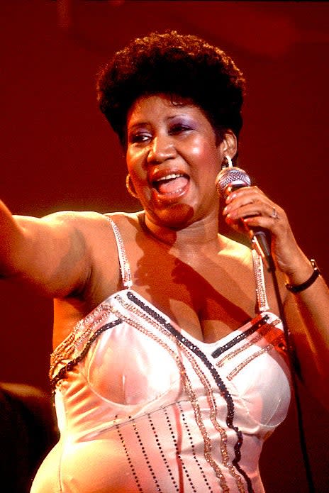 Aretha Franklin performing on stage in a white dress with a microphone