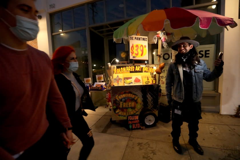 Artist Francisco Palomares stands in front of his converted fruit cart as pedestrians walk past in the Arts District.