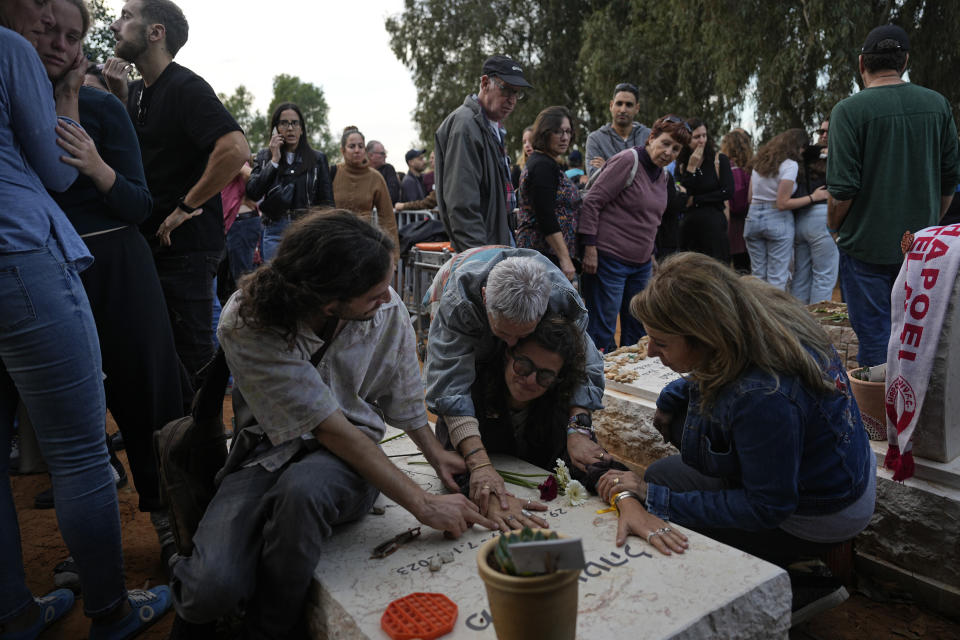 Friends that attended the funeral of 26-year-old Alon Shamriz mourn over the grave of a victim of the Oct. 7th attack buried in the same cemetery in Kibbutz Shefayim, Israel, Sunday Dec. 17, 2023. Shamriz was one of three hostages mistakenly shot to death by Israeli troops Friday in a neighborhood of Gaza City.(AP Photo/Ohad Zwigenberg)