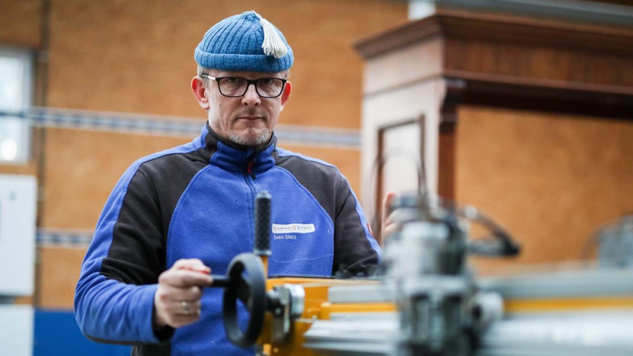 Glasermeister Sven Sterz steht in seiner Werkstatt an einem Glasschneidetisch. Foto: Mohssen Assanimoghaddam