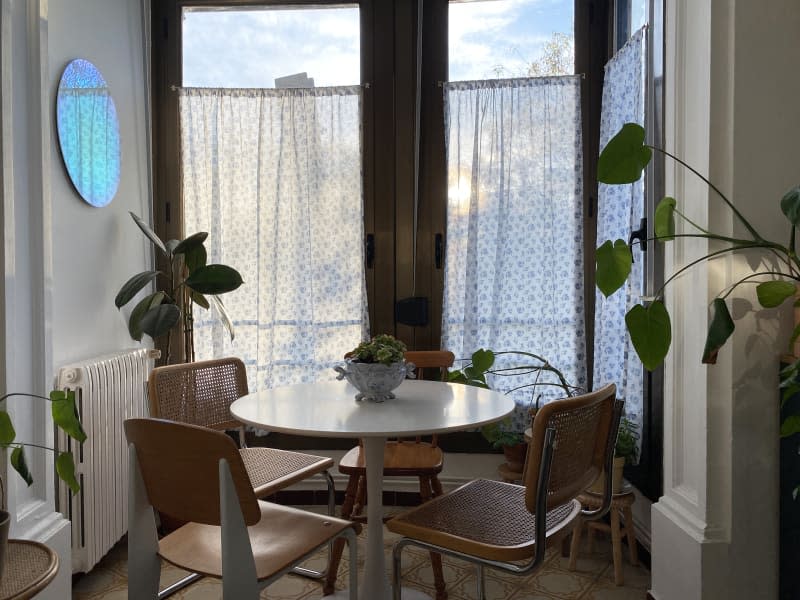 white dining room with large windows, sheer patterned curtains, rattan chairs and round table