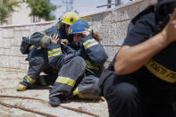 Bomberos israelíes se ponen a cubierto al sonar la sirena antiaérea por los cohetes lanzados desde la Franja de Gaza, en la población israelí de Ashkelon, en el sur del país, el martes 11 de mayo de 2021. (AP Foto/Ariel Schalit)