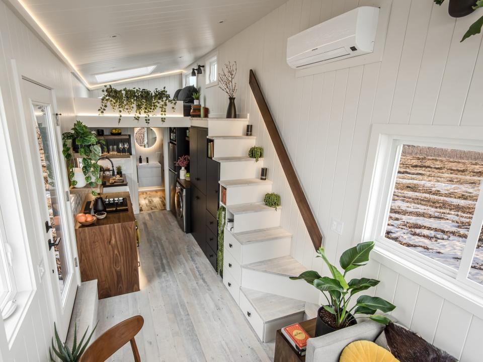 a wide angle view of the tiny home's staircase, loft, kitchen, windows, and entry door