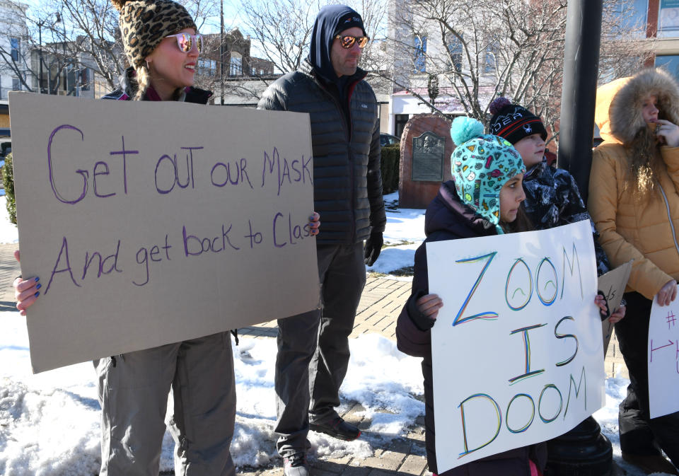 Several people, many without masks, hold signs reading 