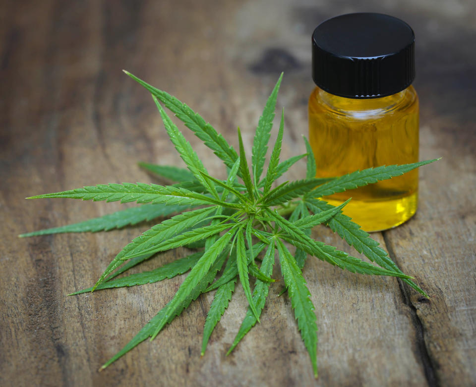 A vial of cannabinoid-based oil next to a group of cannabis leaves on a table.