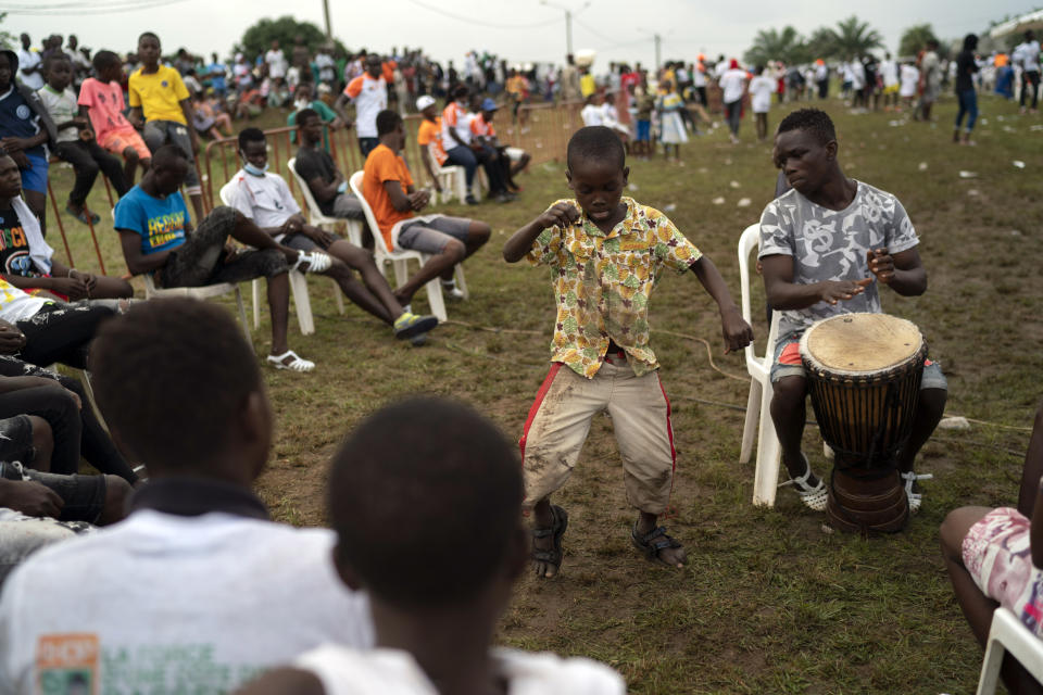 A boy dances as a supporter plays an african percussion instrument before the arrival of the Ivory Coast President Alassane Ouattara at a rally in Anyama, in the outskirts of Abidjan, Ivory Coast, Wednesday, Oct. 28, 2020. Ouattara, who first came to power after the 2010 disputed election whose aftermath left more than 3,000 people dead, is now seeking a third term in office. The candidate maintains that he can serve a third term because of changes to the country's constitution, though his opponents consider his candidacy illegal. (AP Photo/Leo Correa)