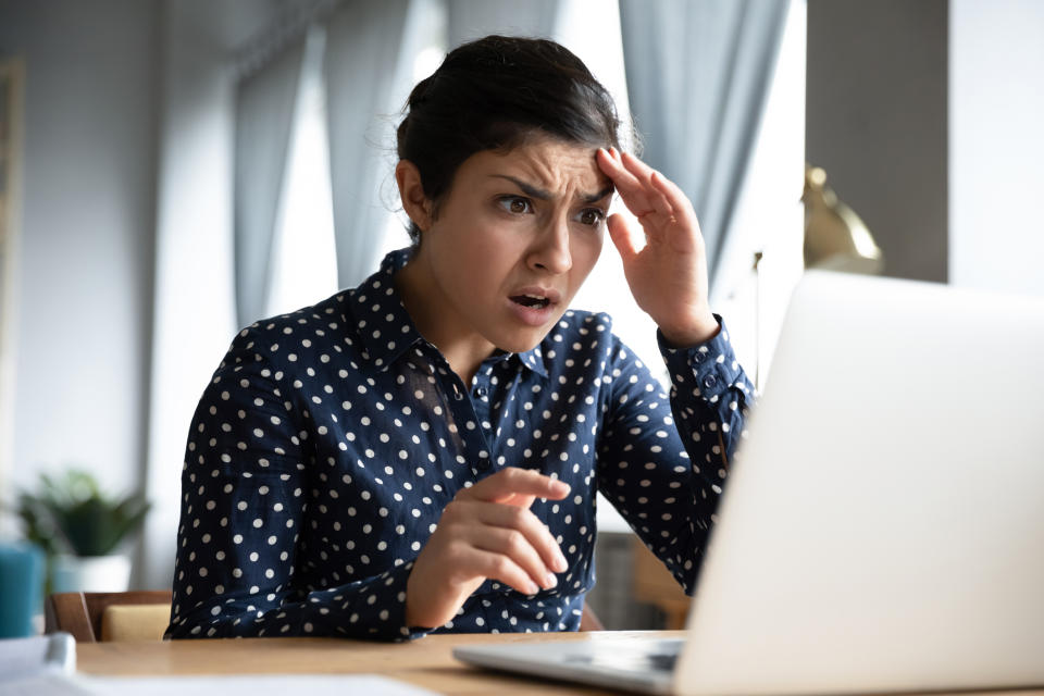 A woman looking shocked at something she's seeing on her laptop