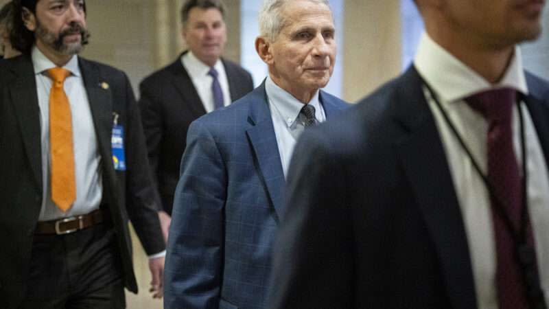 Anthony Fauci walks in the middle of a group of men in suits