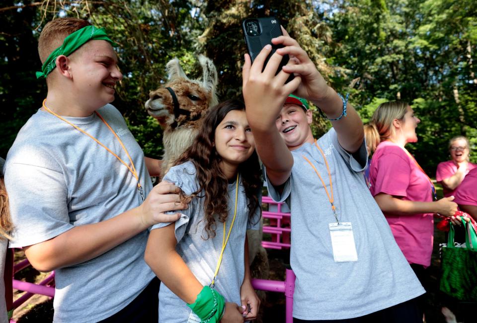 (L to R) Zack Mokachar, 15 and his sister Jenna Mokachar, 12, get in the selfie that camp friend Vaughn Truskin, 12 was taking with Tony the Llama during a petting farm session at the second annual Camp Monarch run by Angela Hospice Center at the Madonna University Welcome Center in Livonia on August 4, 2023. 
The two-day camp is for children ages 5 to 17 who have experienced the loss of a loved one to allow them to bond with other kids their age, talk about grief and get consoling from adults. The three lost their fathers and were attending the camp to help with the healing process.