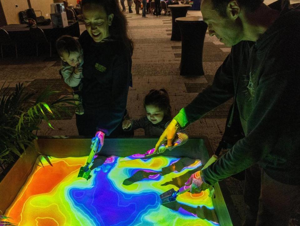 Yael and Josh Dyckman of Eugene, Oregon, and their daughters Ruth, 1, and Amira, 3, move sand into piles to change the topography map at the Sandbox of Life exhibit at Hackfort on Thursday. The interactive activity was sponsored by Sensebellum, a Boise-based digital arts company.