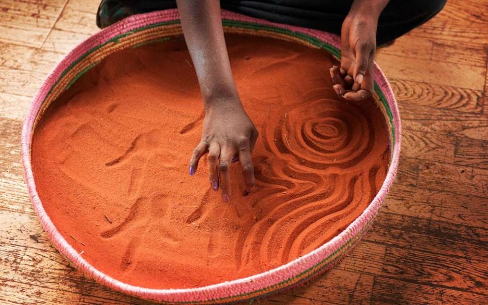 Indigenous artists depict Aboriginal creation myths in sand at Ayers Rock Resort.