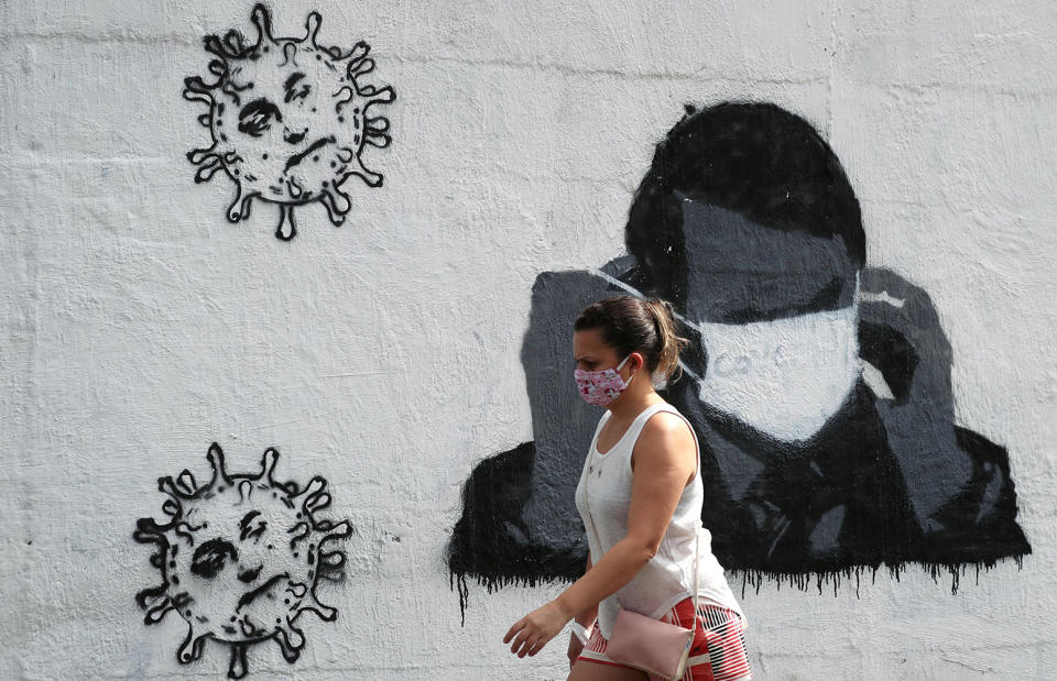 Image: A woman walks past by a graffiti depicting Brazil's President Jair Bolsonaro adjusting his protective face mask and viruses, amid the coronavirus disease (COVID-19) outbreak in Rio de Janeiro, Brazil (Sergio Moraes / Reuters)