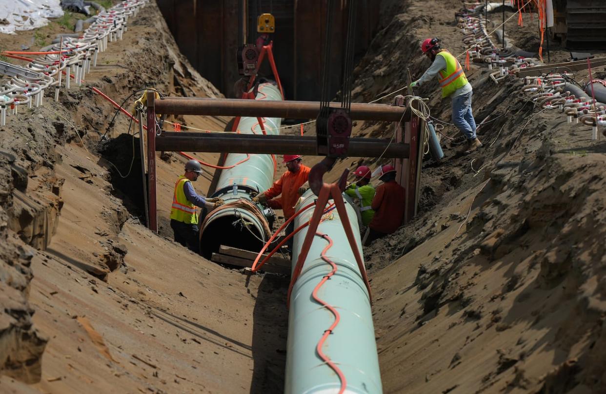 Workers lay pipe during construction of the Trans Mountain pipeline expansion on farmland in Abbotsford, B.C., in this 2023 file photo. (Darryl Dyck/The Canadian Press - image credit)