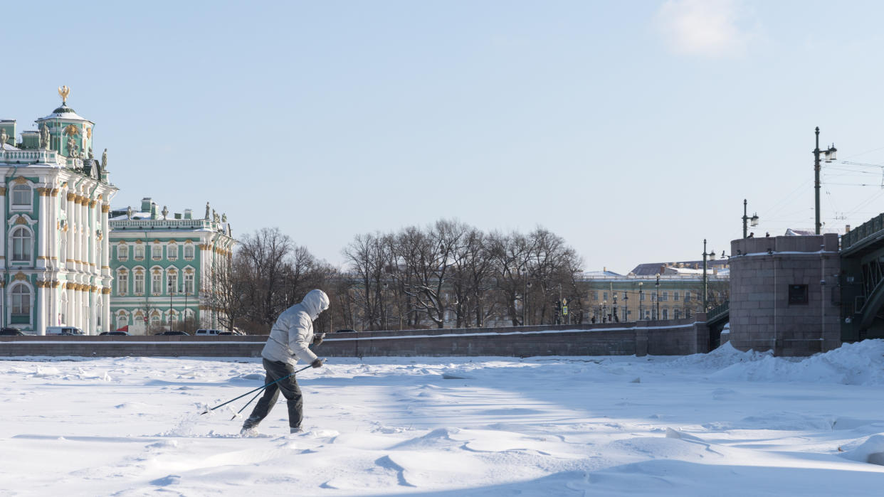 Woman skier riding on ice of the frozen Neva River at sunny day, winter in St.Petersburg, Hermitage on background