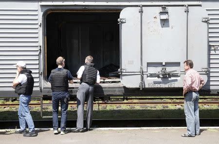 Monitors (L) from the Organization for Security and Cooperation in Europe inspect a refrigerator wagon, which according to employees and local residents contains bodies of passengers of the crashed Malaysia Airlines Boeing 777 plane, at a railway station in the town of Torez, Donetsk region July 20, 2014. REUTERS/Maxim Zmeyev