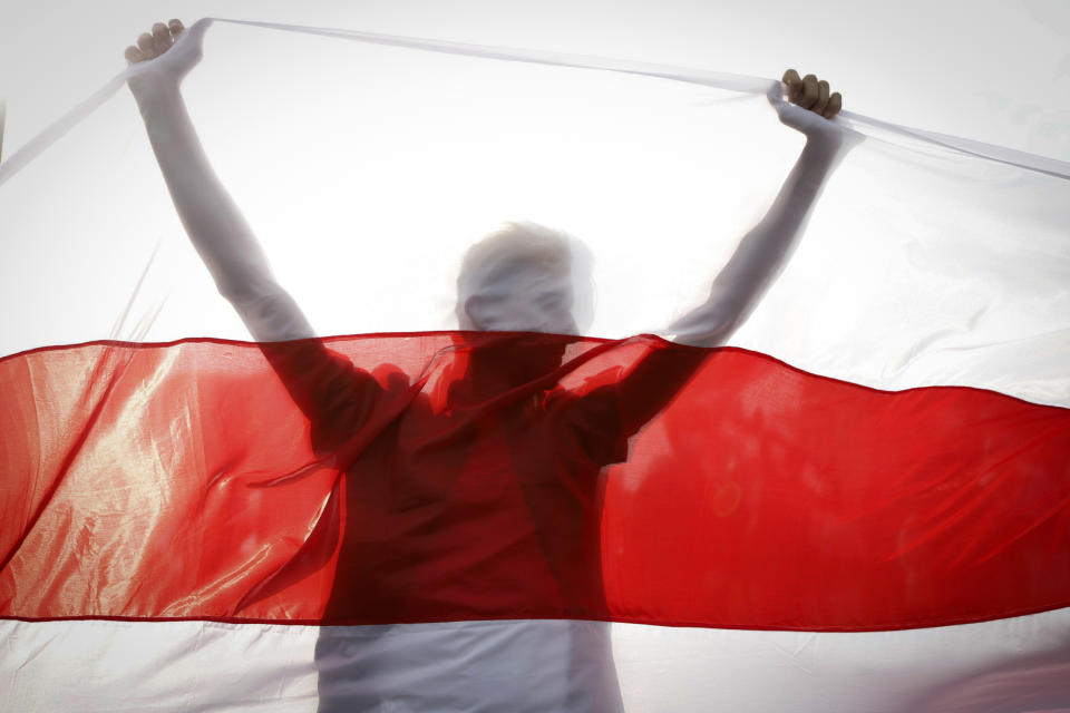 FILE - In this Sunday, Oct. 4, 2020 file photo, a demonstrator is silhouetted by an old Belarusian national flag during a rally in Minsk, Belarus. Hundreds of thousands of Belarusians have been protesting daily since the Aug. 9 presidential election. Belarus President Alexander Lukashenko has relied on massive arrests and intimidation tactics to hold on to power despite nearly three months of protests sparked by his re-election to a sixth term, but continuing protests have cast an unprecedented challenge to his 26-year rule. (AP Photo, File)