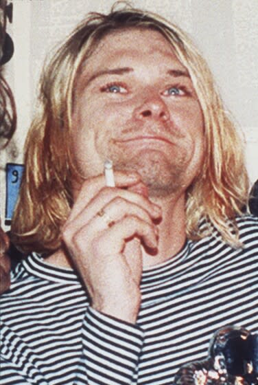 A photo of a shaggy-haired man smiling and smoking a cigarette