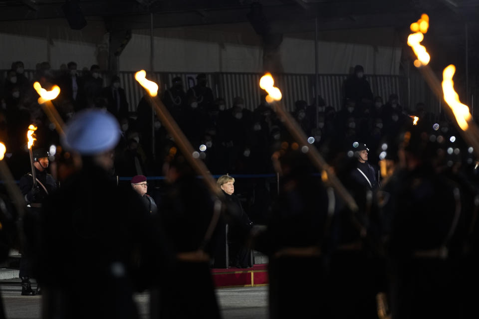 Chancellor Angela Merkel, center, attends in a Grand Tattoo ceremony to mark the farewell of her chancellorship in Berlin, Germany, Thursday, Dec. 2, 2021. With one week left before Merkel steps aside, she is being treated to a traditional send off involving the military ceremony with a brass band playing her choice of music. (AP Photo/Markus Schreiber)