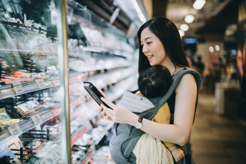 Young Asian mother grocery shopping with little daughter and choosing for fresh fish in the supermarket