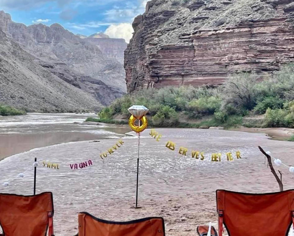 A tacky wedding setting with three red camping chairs and two signs, outside, by a river.